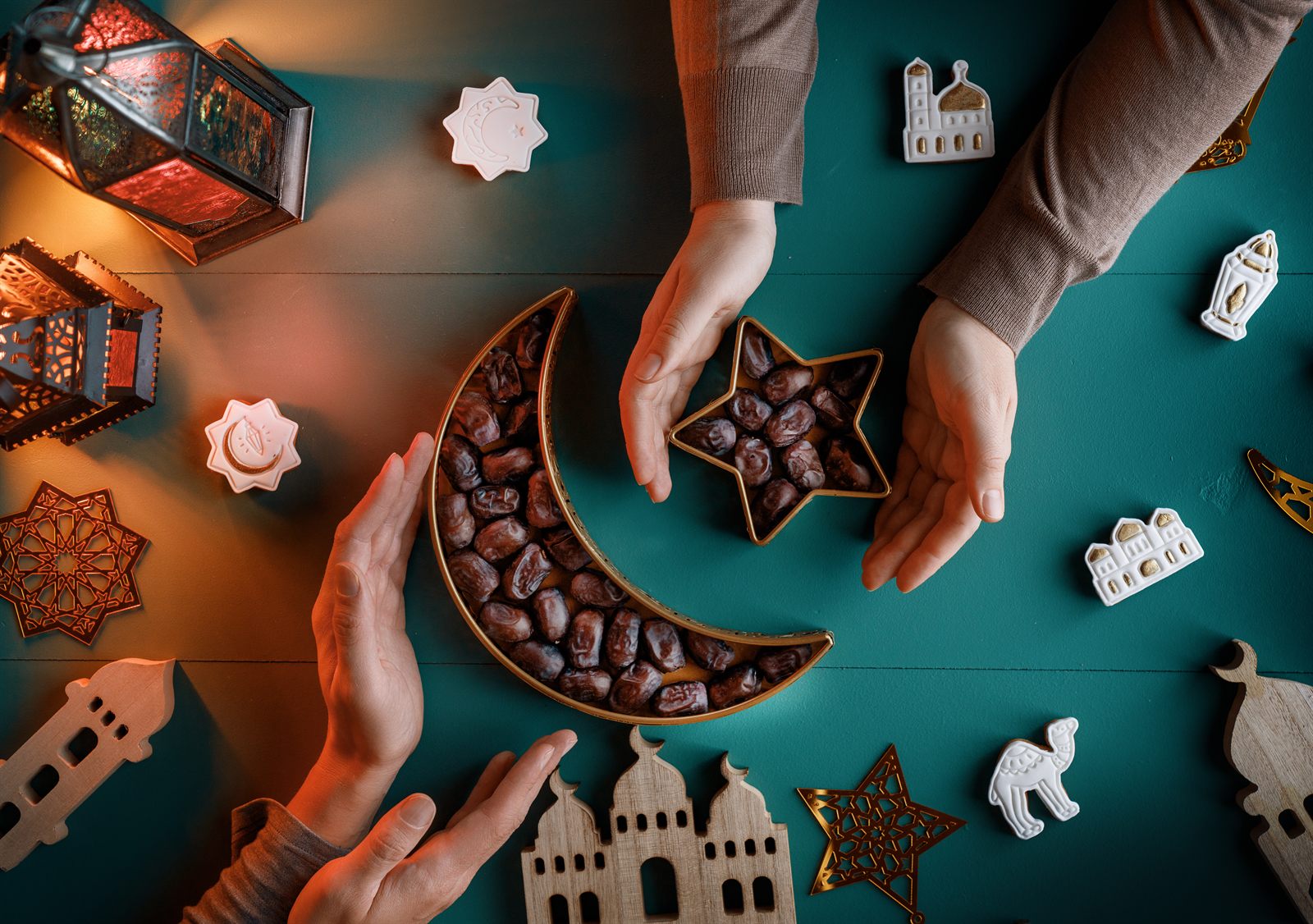 Ramadan and Eid table setting with dates, lanterns and hands reaching in