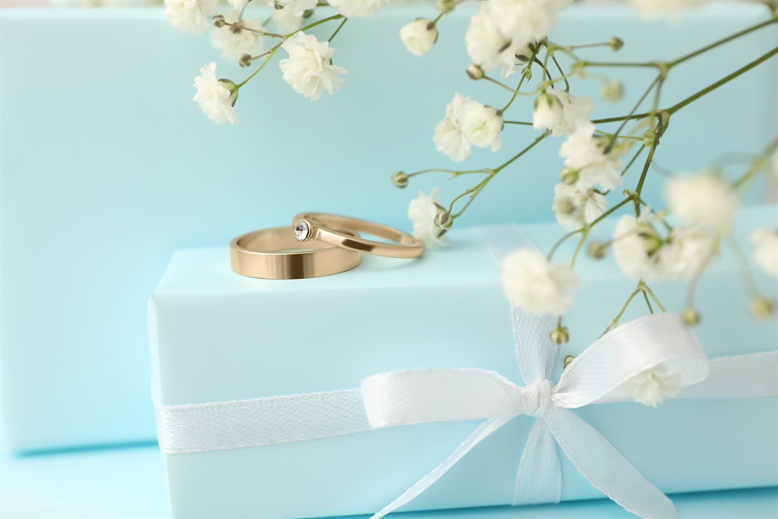 Wedding rings resting on a wrapped gift box with ribbon and flowers