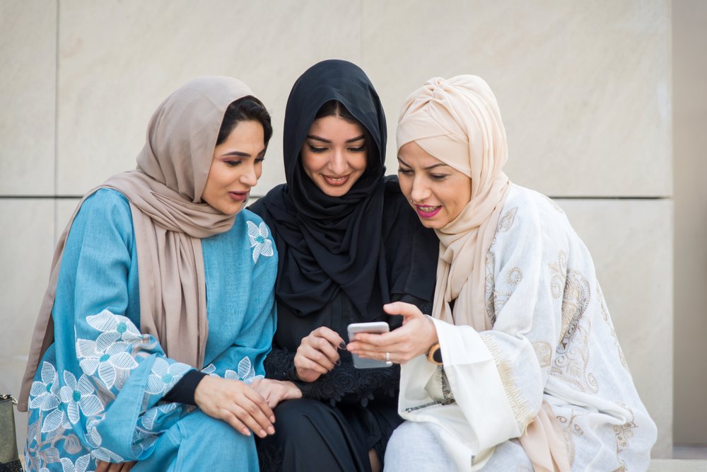 Three women looking together at Salah guidance on a phone