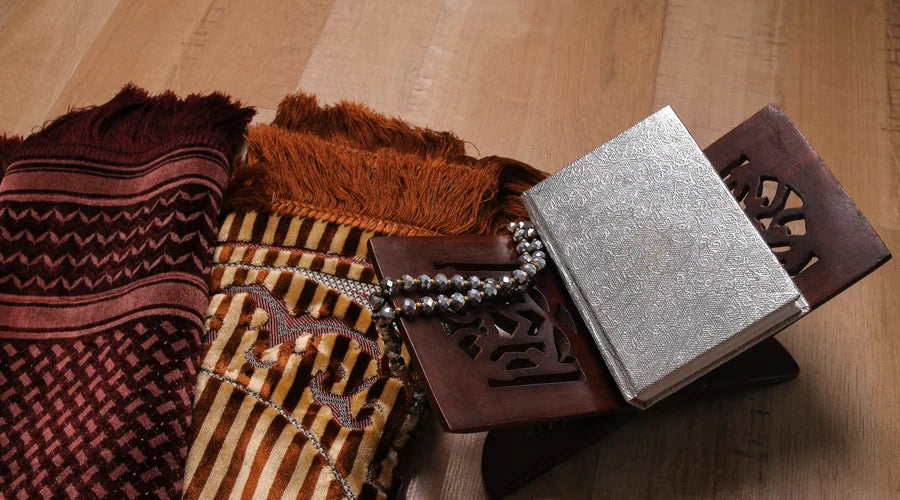 Folded traditional prayer mats beside a Quran on its stand and a string of prayer beads